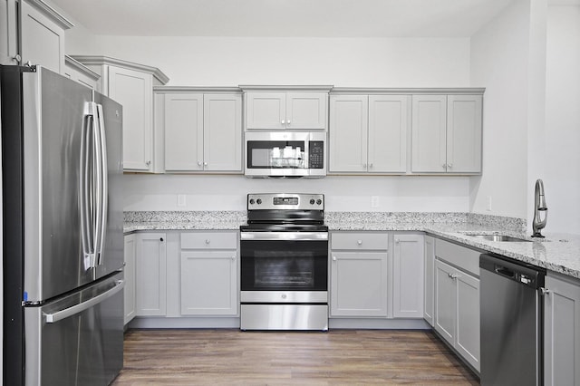 kitchen with stainless steel appliances, wood finished floors, gray cabinetry, a sink, and light stone countertops