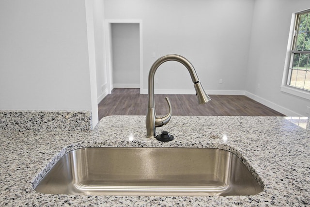 room details with light stone counters, a sink, baseboards, and wood finished floors