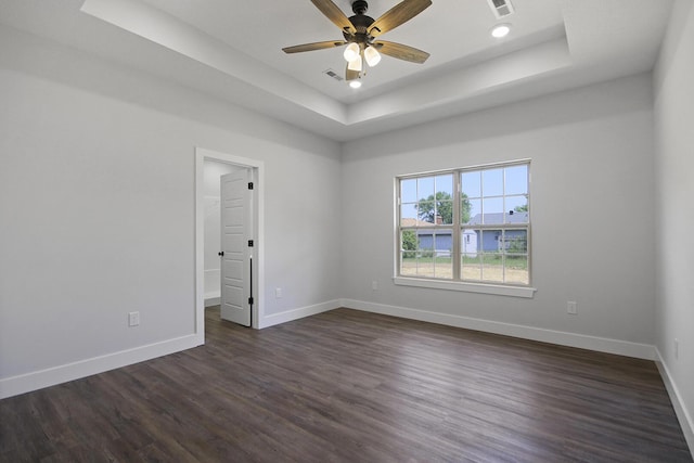 empty room featuring a tray ceiling, dark wood finished floors, visible vents, ceiling fan, and baseboards