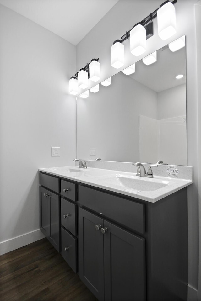 full bathroom featuring double vanity, baseboards, a sink, and wood finished floors