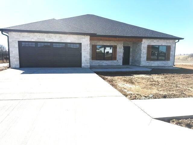 view of front facade featuring a garage, concrete driveway, a shingled roof, and stone siding