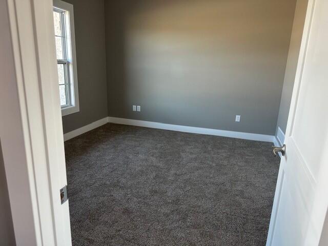 spare room with dark carpet and baseboards