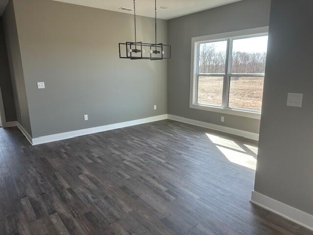 unfurnished dining area featuring a chandelier, dark wood finished floors, and baseboards