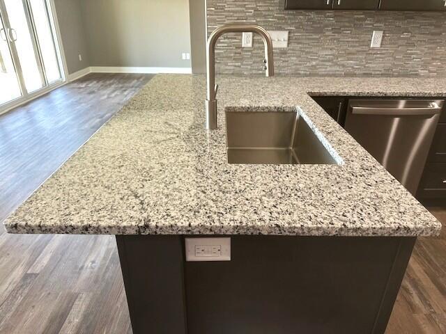 room details featuring dark wood finished floors, backsplash, stainless steel dishwasher, a sink, and light stone countertops