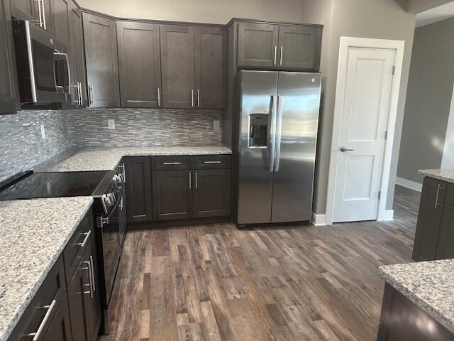 kitchen featuring stainless steel appliances, dark brown cabinetry, backsplash, and dark wood-style floors