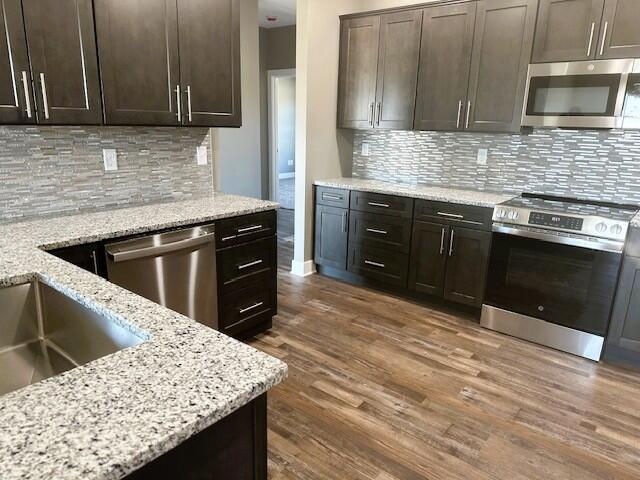 kitchen with stainless steel appliances, light stone countertops, dark brown cabinetry, and wood finished floors