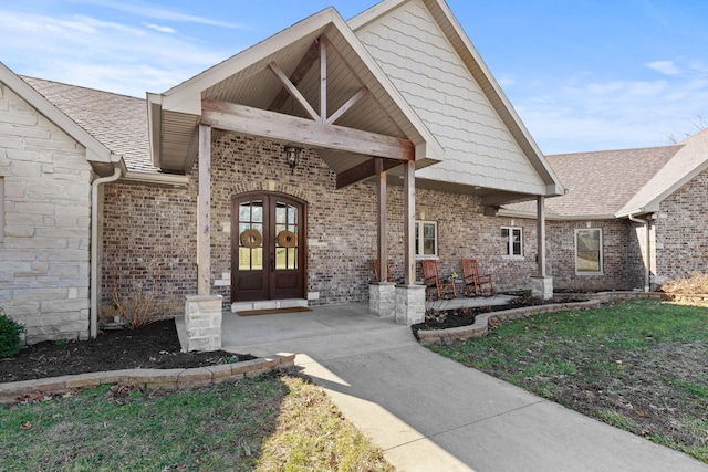 view of exterior entry featuring french doors, stone siding, brick siding, and a shingled roof