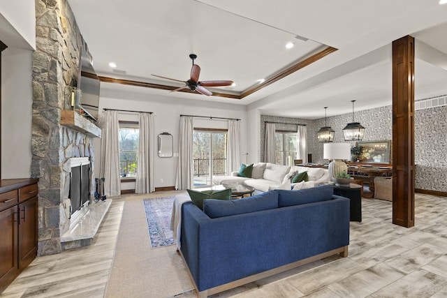 living room featuring ceiling fan, baseboards, a fireplace, light wood-style floors, and a raised ceiling