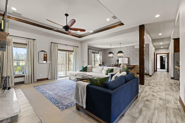 living room with light wood-type flooring, visible vents, a tray ceiling, ceiling fan, and an accent wall