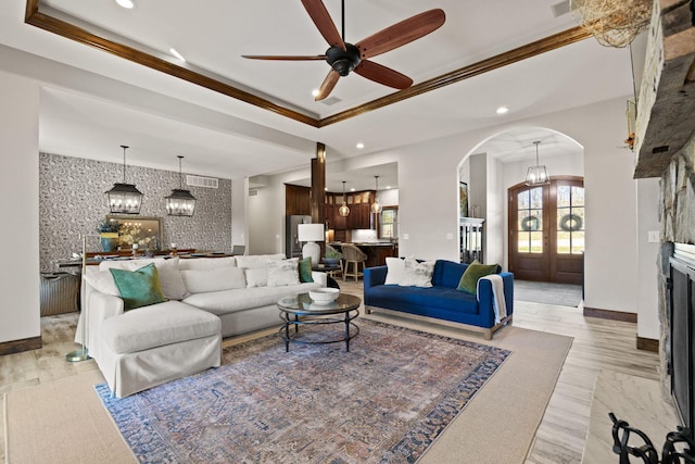 living room featuring a raised ceiling, recessed lighting, arched walkways, and baseboards