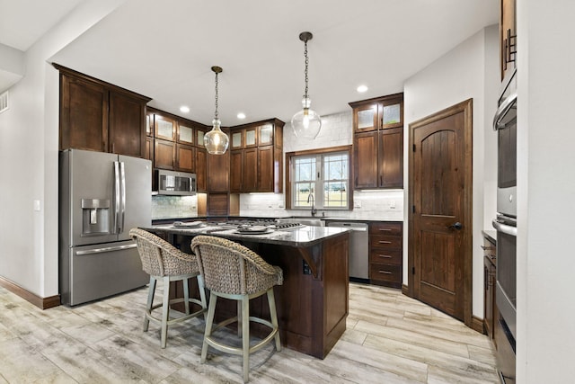 kitchen with a breakfast bar area, a sink, appliances with stainless steel finishes, backsplash, and a center island