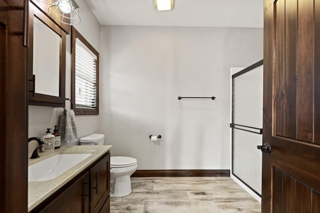 bathroom with toilet, wood finished floors, a shower stall, baseboards, and vanity