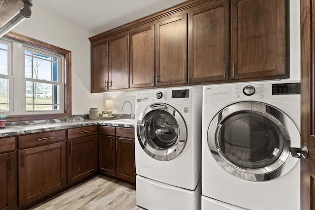 laundry room with washer and clothes dryer, cabinet space, light wood-type flooring, and a sink