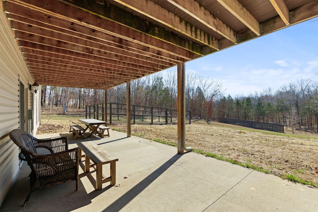 view of patio with outdoor dining space, a wooded view, and fence