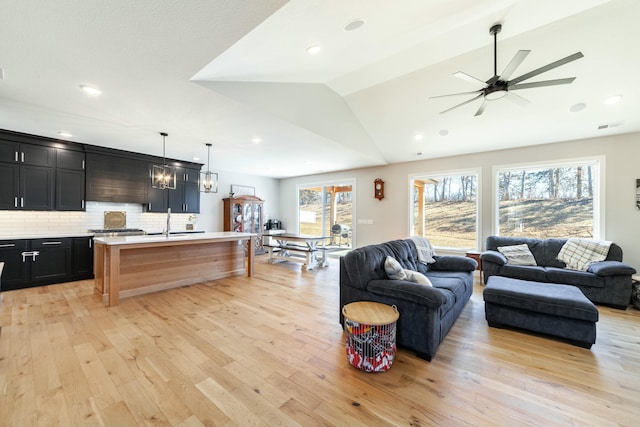 living area featuring light wood-type flooring, lofted ceiling, visible vents, and ceiling fan