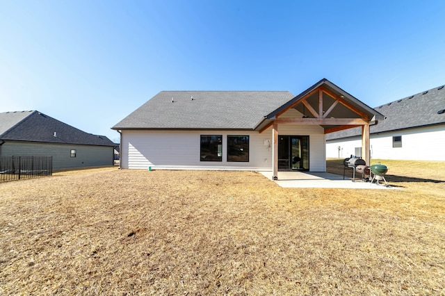 rear view of property with roof with shingles, a patio, and a lawn