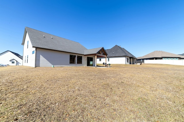 rear view of house with a patio area, a lawn, and roof with shingles