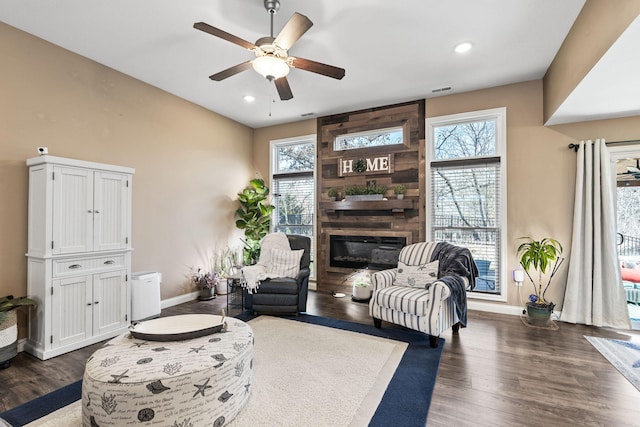 living area with ceiling fan, a fireplace, dark wood-style flooring, and baseboards