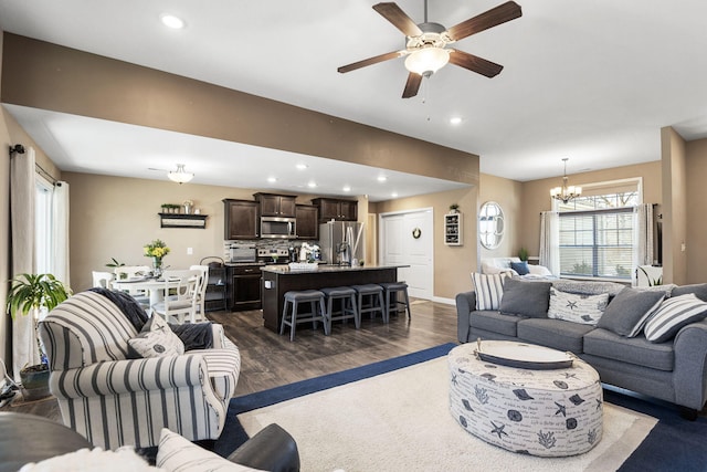 living room with dark wood-style floors, recessed lighting, ceiling fan with notable chandelier, and baseboards