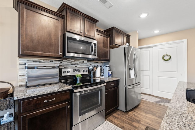 kitchen with visible vents, dark wood-style flooring, dark brown cabinets, appliances with stainless steel finishes, and backsplash