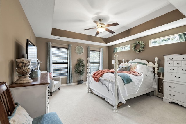 bedroom with a ceiling fan, a tray ceiling, light colored carpet, and baseboards