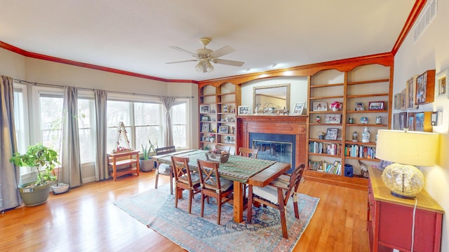 dining room with crown molding, visible vents, a ceiling fan, a glass covered fireplace, and wood finished floors