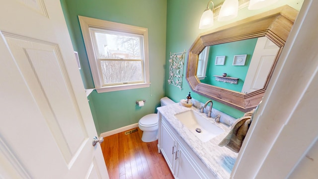 half bathroom featuring baseboards, visible vents, toilet, hardwood / wood-style floors, and vanity