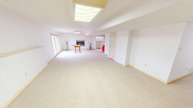 below grade area featuring a glass covered fireplace, carpet flooring, and baseboards