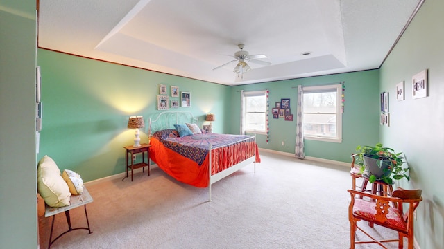 carpeted bedroom featuring a tray ceiling, ceiling fan, and baseboards