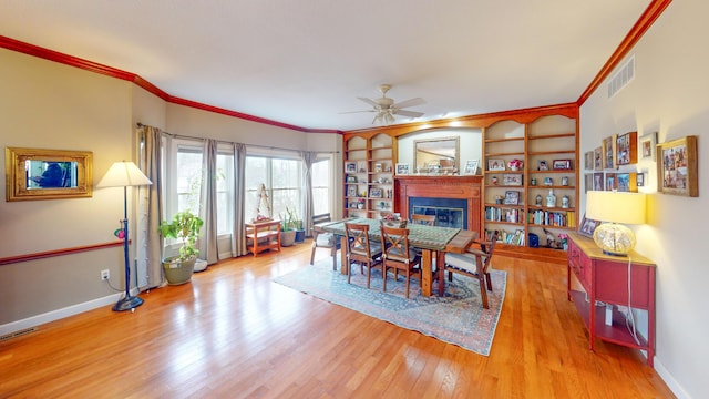 dining room featuring visible vents, ornamental molding, wood finished floors, and a glass covered fireplace