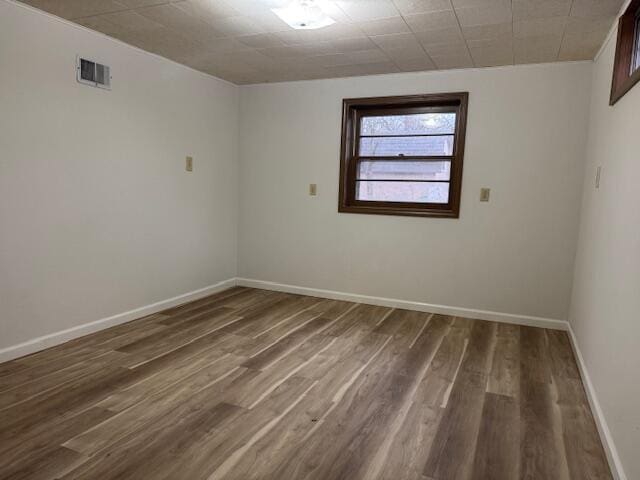 empty room featuring wood finished floors, visible vents, and baseboards