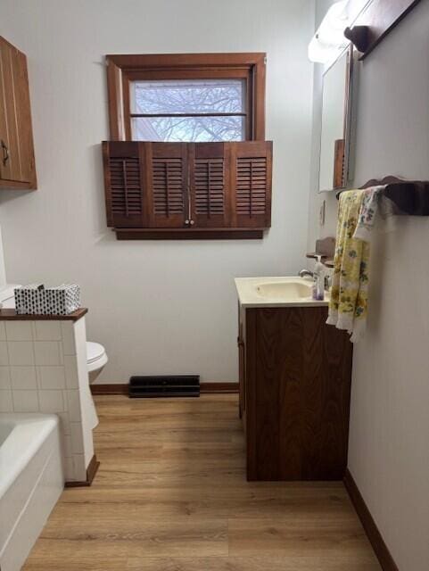 bathroom with a garden tub, toilet, wood finished floors, baseboards, and vanity