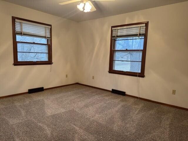 carpeted empty room featuring a wealth of natural light, visible vents, ceiling fan, and baseboards