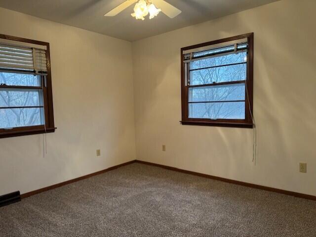 carpeted spare room with visible vents, a healthy amount of sunlight, baseboards, and ceiling fan