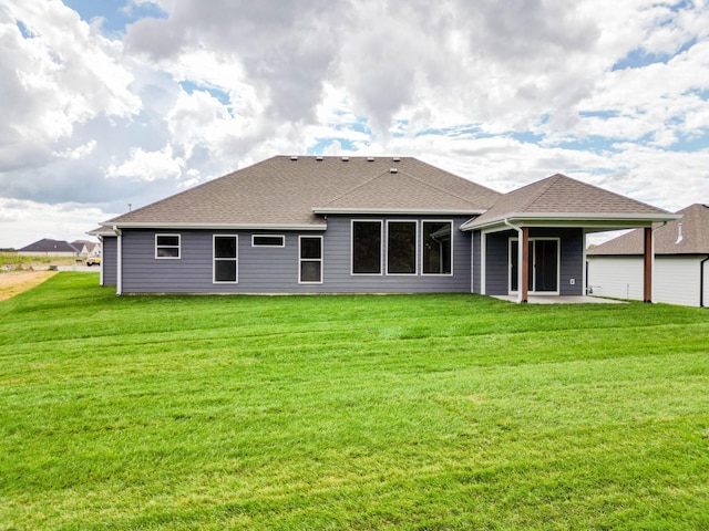 back of house with roof with shingles, a lawn, and a patio area