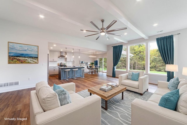 living area featuring baseboards, visible vents, beam ceiling, and wood finished floors