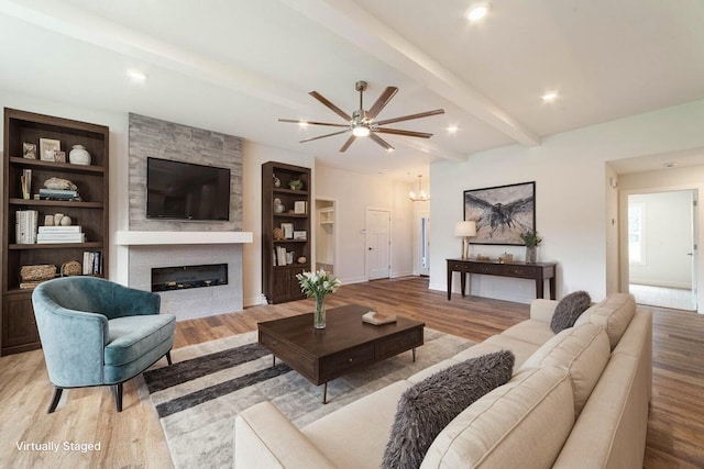 living area featuring beam ceiling, a large fireplace, built in features, and light wood finished floors