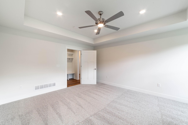 carpeted spare room featuring a tray ceiling, visible vents, baseboards, and recessed lighting