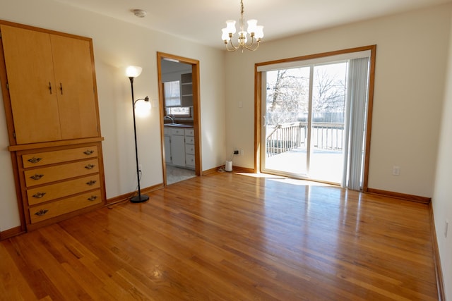 unfurnished bedroom with baseboards, a notable chandelier, light wood-style flooring, and access to outside