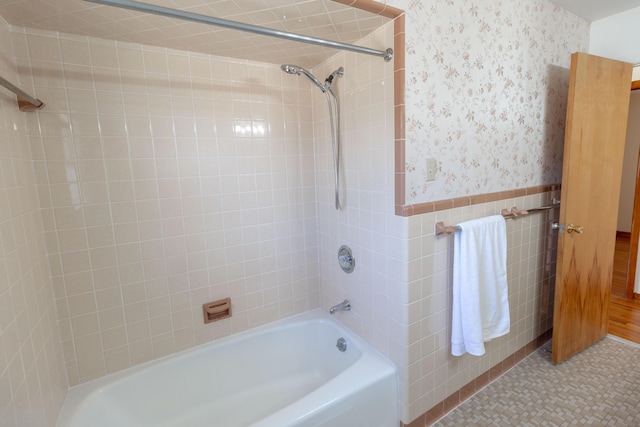 full bathroom featuring tile walls,  shower combination, wainscoting, and wallpapered walls