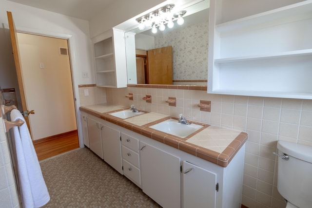 bathroom featuring a sink, visible vents, double vanity, and wallpapered walls