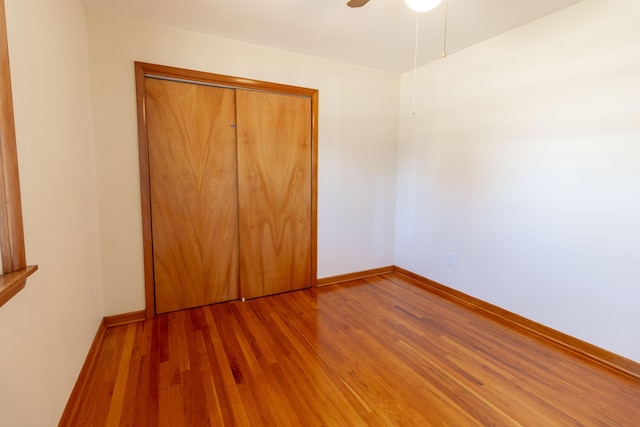 unfurnished bedroom featuring ceiling fan, a closet, baseboards, and wood finished floors