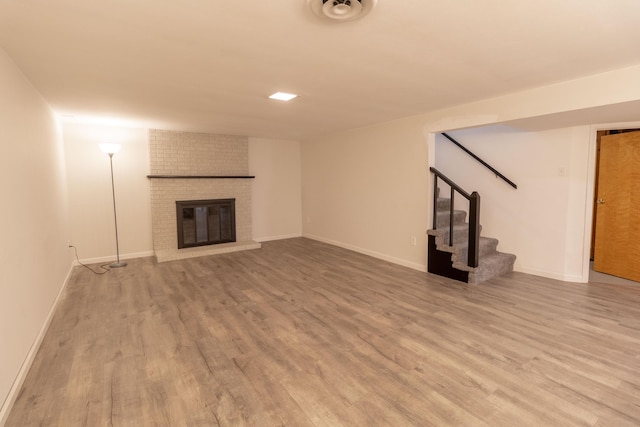 unfurnished living room featuring stairs, a brick fireplace, wood finished floors, and visible vents