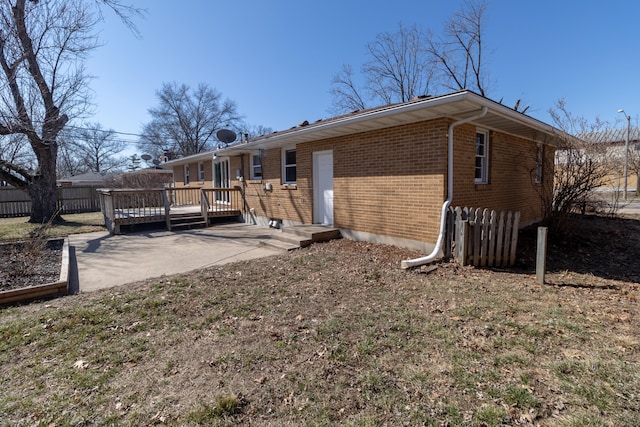 rear view of property featuring brick siding, a patio area, a deck, and fence