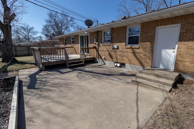 rear view of property with brick siding, fence, a wooden deck, a patio area, and driveway