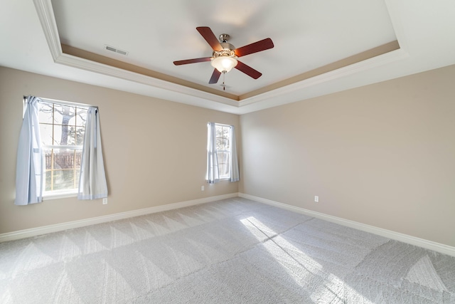 spare room with a tray ceiling, baseboards, visible vents, and a ceiling fan