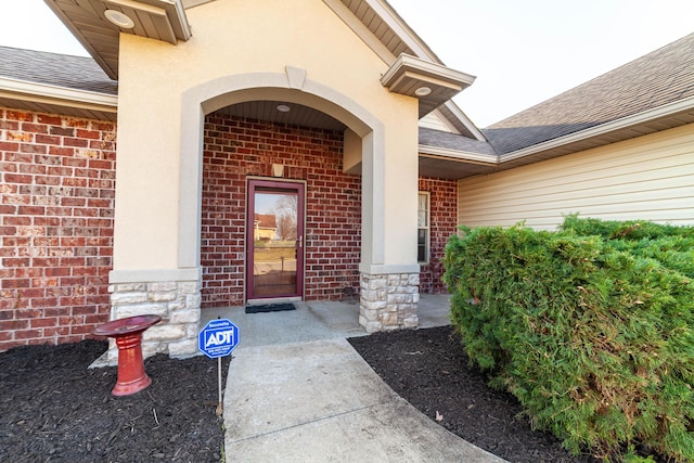 view of exterior entry featuring brick siding and a shingled roof