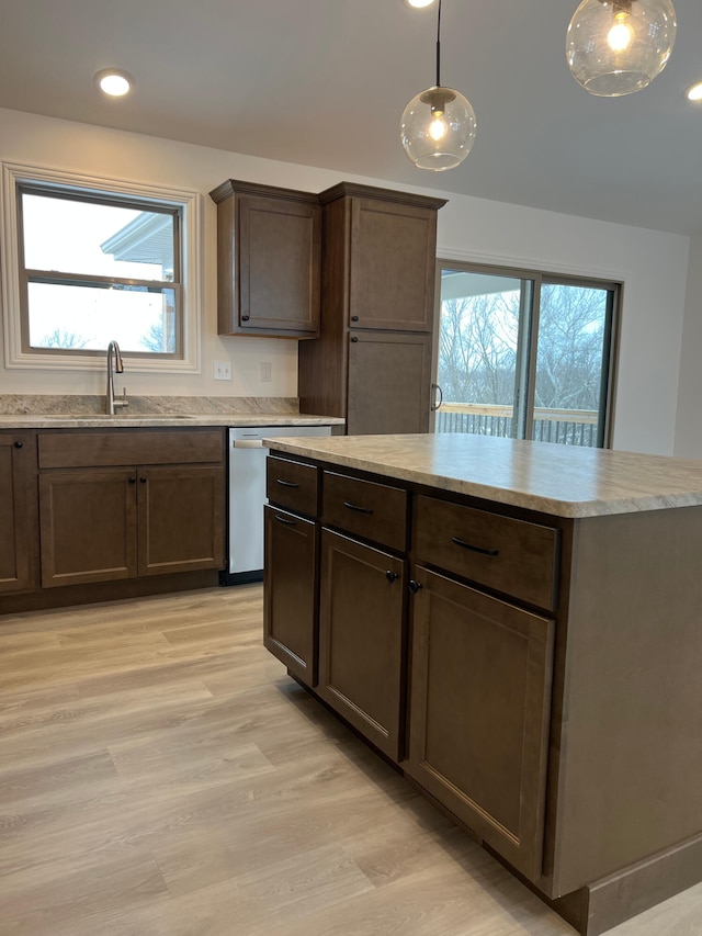 kitchen with hanging light fixtures, light wood finished floors, a sink, and dishwasher