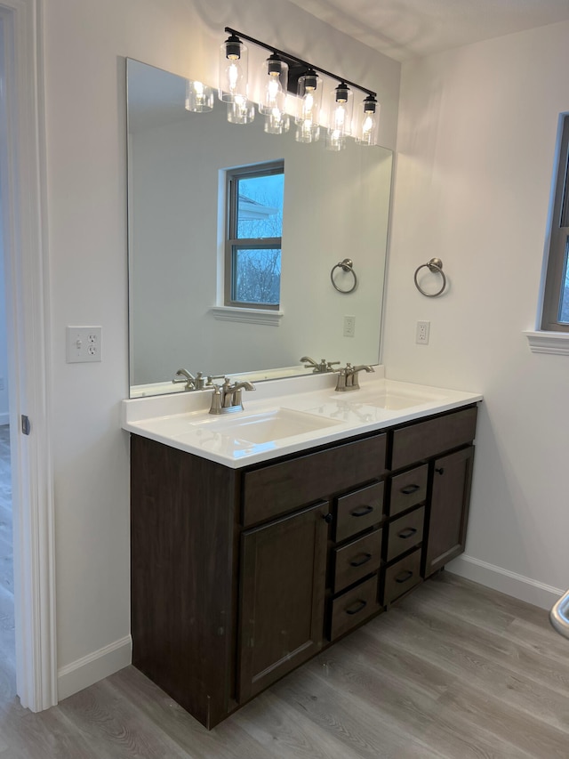 bathroom featuring double vanity, wood finished floors, a sink, and baseboards