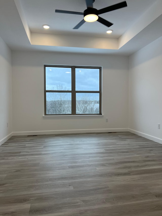 unfurnished room featuring ceiling fan, recessed lighting, wood finished floors, baseboards, and a raised ceiling